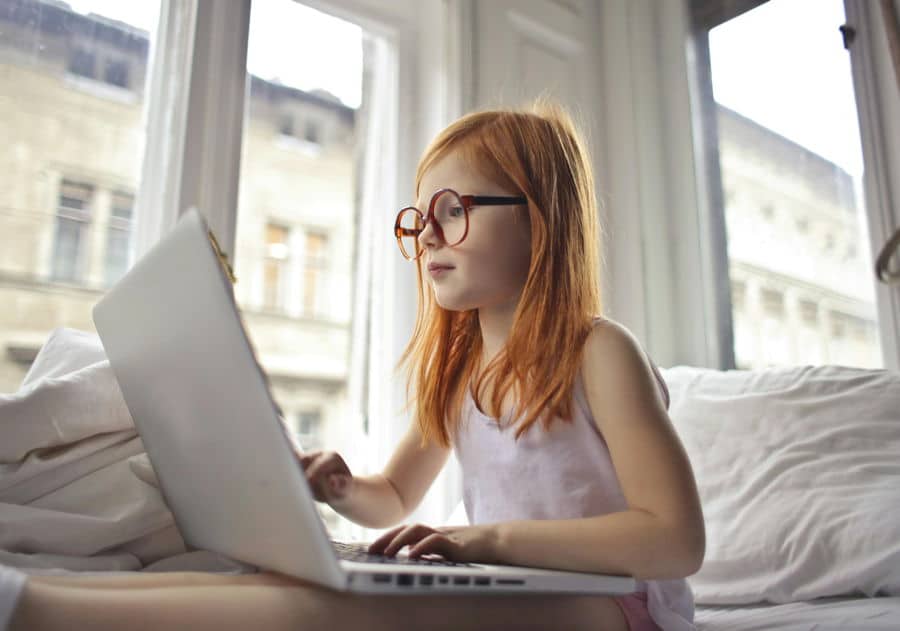 Ein etwa zehn Jahre altes rothaariges Mädchen mit Brille sitzt an einem Laptop und sucht oder betrachtet etwas im Internet.
